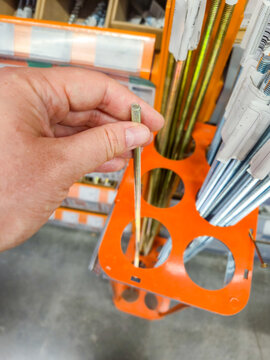 Hand holding a threaded metal rod in a hardware store aisle