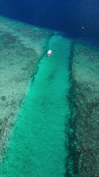 Boat floating, in tropical reef, with boat, reef, from a aerial view perspective, with blue, green accents, and relaxing holiday mood, showing nearby objects and surrounding setting.