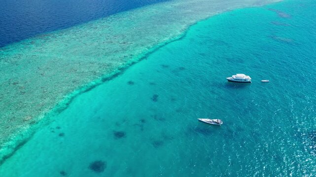 Aerial view of a boat gently floating on tranquil tropical waters in the Maldives, surrounded by sandy reefs and vibrant blue-green hues, creating a serene and relaxing holiday travel id.