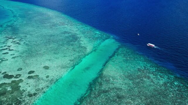 A serene and tranquil aerial view of a boat on vibrant tropical reefs in the Maldives, captured from a high-altitude perspective. The scene showcases the beauty of the transparent water.
