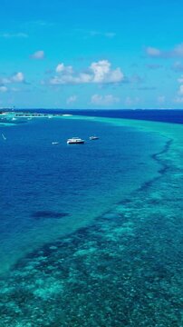 Boat floating, in tropical reef, with boat, reef, from a aerial view perspective, with blue, green accents, and relaxed serene mood, showing nearby objects and surrounding setting, vertical video