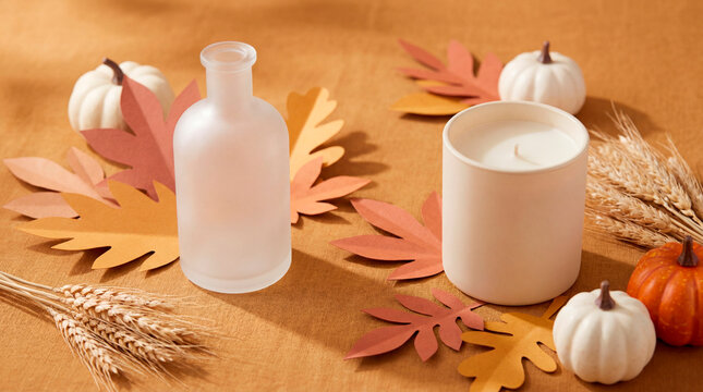 Autumn candle and frosted bottle mockup with paper leaves pumpkins and wheat on ochre backdrop