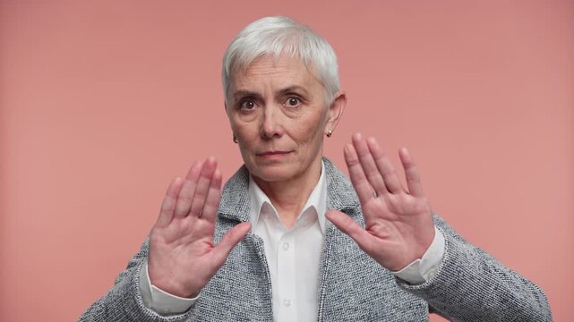 Senior Woman Making Stop Hand Gesture on Pink Background