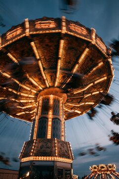 A long exposure photograph of a brightly lit carousel swing ride at a fairground during twilight.