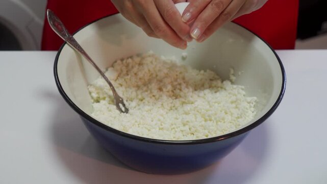 Careful hands prepare fresh curd cheese inside a large blue bowl. This quiet cooking happens at a white kitchen table, bringing a comforting and peaceful feeling of home.
