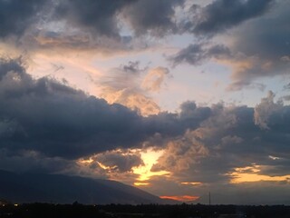 Fototapeta premium Dramatic sunset sky with golden clouds over mountain silhouette, Yunnan twilight landscape