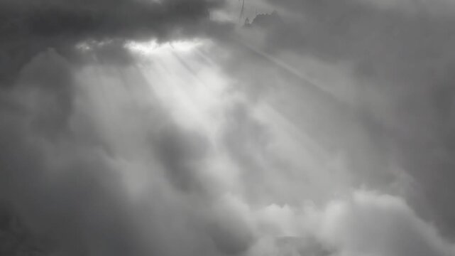 Sunrays piercing heavy clouds in monochrome style on a moody sky background, conveying a concept of hope and renewal