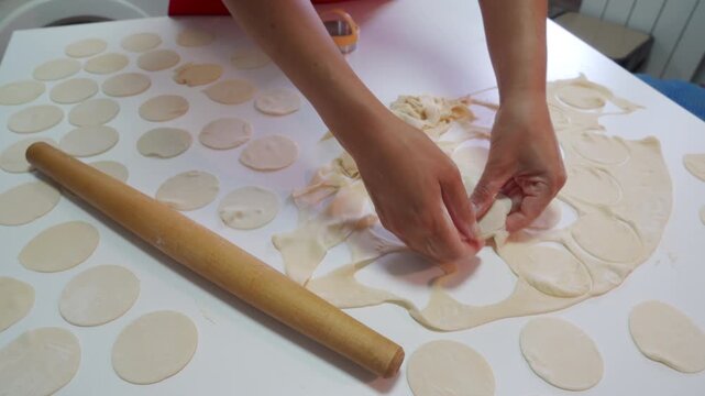 Careful hands gently separate round dough pieces on a white kitchen table next to a wooden rolling pin. This peaceful cooking tradition brings a satisfying and comforting feeling to the cozy home.