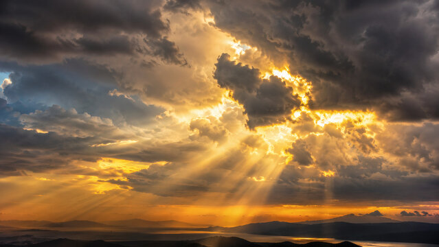Dramatic storm clouds with golden sun rays breaking through, epic sky with amber light