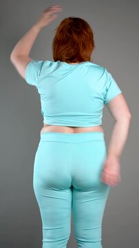 Unrecognizable curvy woman performs exercises for muscles of upper back, arms and shoulder joint, posture correction and physical therapy concept on gray background