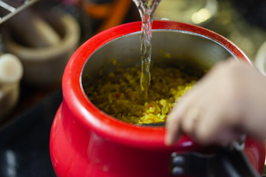 Indian woman adding water to khichdi in a pressure cooker