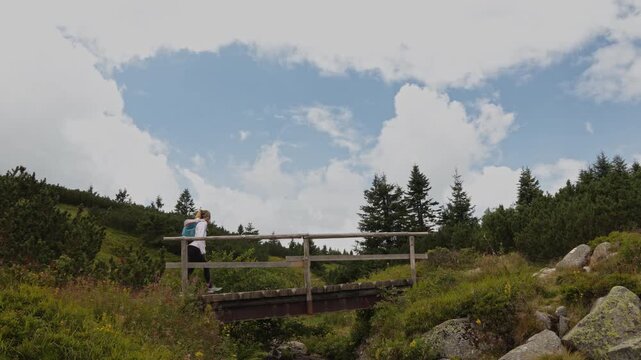 Woman with a backpack hiking across a wooden bridge over the Elbe river in Krkonose National Park, Czech Republic