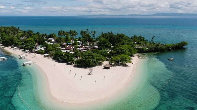 Coastal village with palm trees and white sandy shore along a turquoise sea in Tulang Diot Island. Camotes, Philippines.