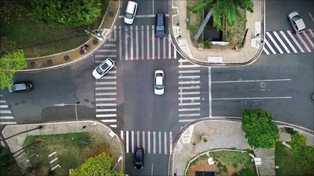 Aerial view of urban intersection with cars and motorcycles crossing zebra stripes in city traffic.
