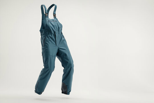 Teal work overalls hanging on white wall, durable canvas bib pants with pockets and straps, minimal studio apparel photo for retail catalog