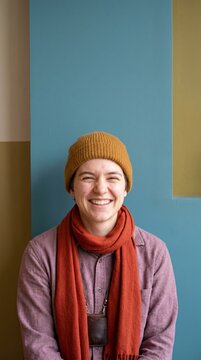 Smiling young person in a beanie and scarf laughing against a colorful wall