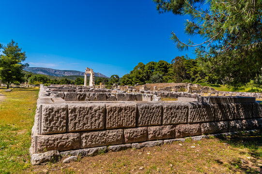 A view past a wall across ruins at the archaeological ruins of the Sanctuary of Asclepius at Epidaurus in early summertime
