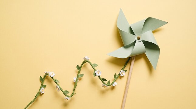Paper pinwheel and floral vine stem top view on yellow background studio shot for clean energy and environmental growth concept