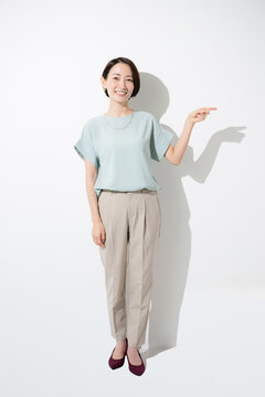 Full-body shot of a Japanese woman in a short-sleeved top, smiling and pointing to provide directions against a white background; looking directly at the camera&mdash;an illustrative image for announcements