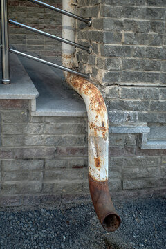 A fragment of an old downpipe on a wall on a summer day