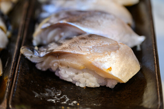 Close up of seared pickled mackerel nigiri sushi served on dark ceramic plate. Japanese aburi shime saba sushi delicacy concept. High angle view with selective focus.