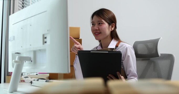 Warehouse employee processing inventory, checking shipping documents, updating stock records, and managing parcel information at an office workstation for logistics and warehouse operations.
