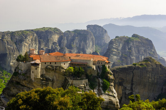 The Monastery of Great Meteoron perched atop a rock formation in Meteora, Greece, under a hazy sky.