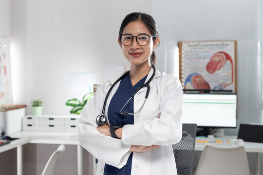 Confident smiling female doctor standing with crossed arms in a modern medical office. Professional healthcare worker wearing a white coat, stethoscope, and eyeglasses, representing medical expertise,