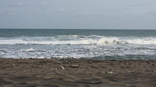Plastic trash and debris scattered on a dark sand beach with ocean waves of the Indian Ocean during late afternoon, environmental pollution and ocean conservation concept.