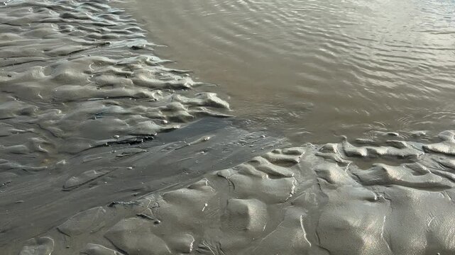 Rippling seawater flowing over textured wet beach sand