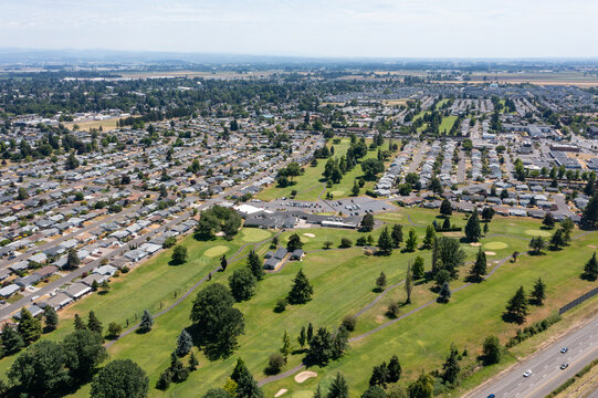 Aerial drone photo of Woodburn, Oregon, USA featuring residential neighborhoods, green parks, golf course, and surrounding Willamette Valley landscape on a clear summer day