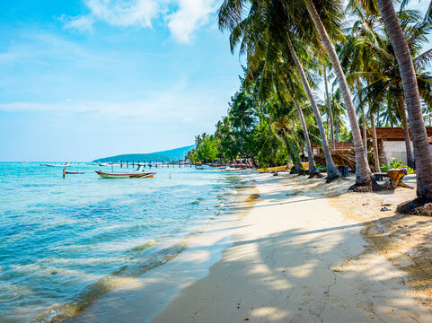 Tropical beach in Karimunjawa. Jepara. Jawa Tengah. Indonesia. Showing turquoise water. White sand. And leaning palm trees under a bright blue sky. With a traditional fishing boat floating peacefully