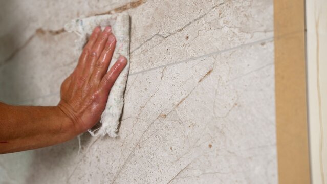 Hand polishing a marble surface with a cloth. A worker wipes down ceramic tiles after grouting them with epoxy grout.