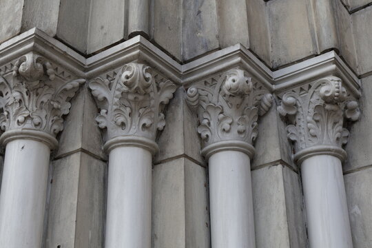 Four ornate white marble Corinthian columns each with unique different floral carvings on capitals, classical historic building facade architectural detail, elegant decorative stone pillars close-up v
