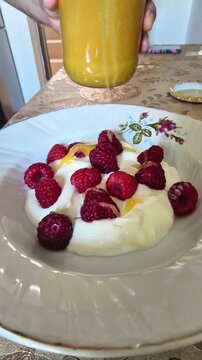 Fresh raspberries falling into creamy yogurt creating healthy breakfast in natural light beautifully