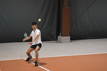 Obraz premium Young Asian Man Playing Tennis on Indoor Clay Court with Racket in Action