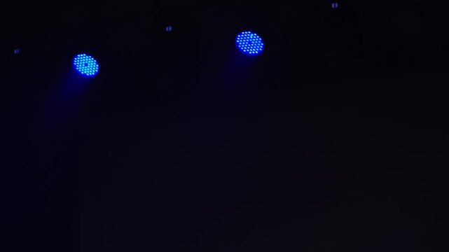 Bright theatrical spotlights shining through atmospheric haze, dynamically changing colors from crisp white to warm orange in a dark event venue.