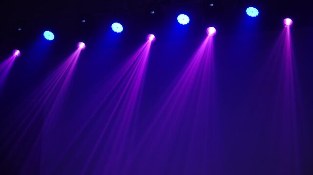 Bright theatrical spotlights shining through atmospheric haze, dynamically changing colors from crisp white to warm orange in a dark event venue.