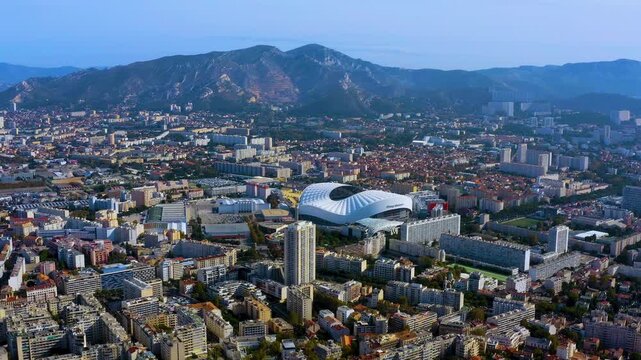 Aerial drone view of Stade Velodrome football stadium and the Marseille cityscape with residential districts and Provence mountains in the background, southern France, in daytime.