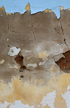 Weather beaten decaying multi-layer wall surface with cracked peeling paint revealing damaged cement layer and rough worn red brick with mortar