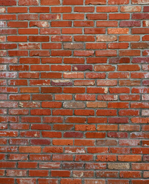 Weathered red brick and mortar wall surface with varied red bricks, occasional tan bricks, aged and worn bricks with cracks, chips and white mineral deposits