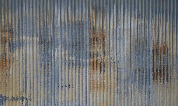 Weathered blue tinted corrugated tin metal siding with rust pitting dents holes white mineral deposits and worn light yellow paint on galvanized vertical ridged surface