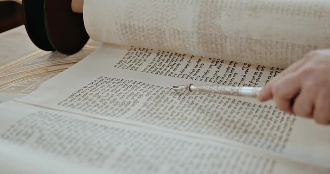 Hand using silver yad pointer to read Hebrew Torah scroll