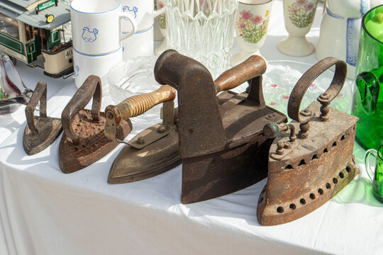 XALO, SPAIN - JUNE 20, 2026.Row of antique cast iron flatirons displayed on a white table at a flea market on a sunny day