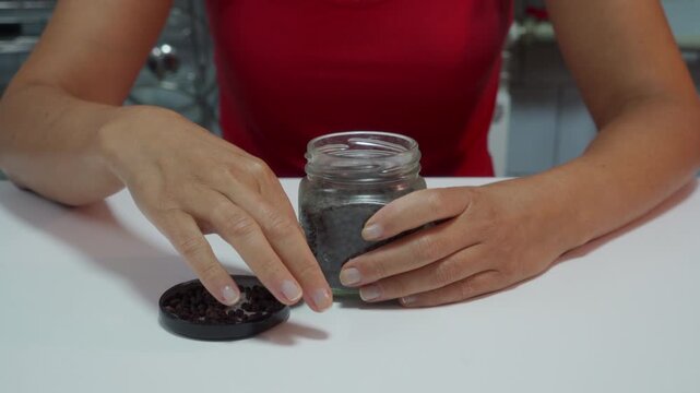 A peaceful woman gently checks black peppercorns from the Piper nigrum plant. She sits calmly at a clean white table indoors, feeling content with her task.