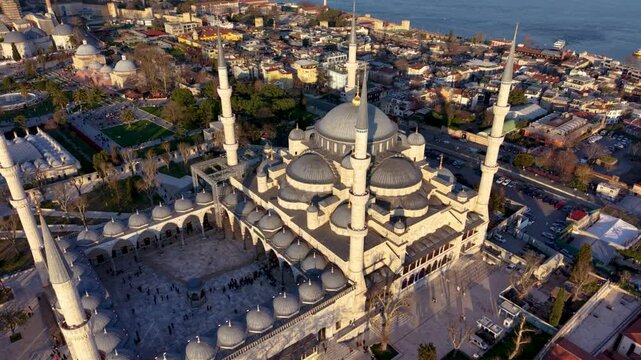 Spectacular aerial drone view of the Blue Mosque (Sultan Ahmed Mosque) in Istanbul, Turkey, with Hagia Sophia, the Bosphorus, and the modern city skyline in the background. Golden hour lighting highli