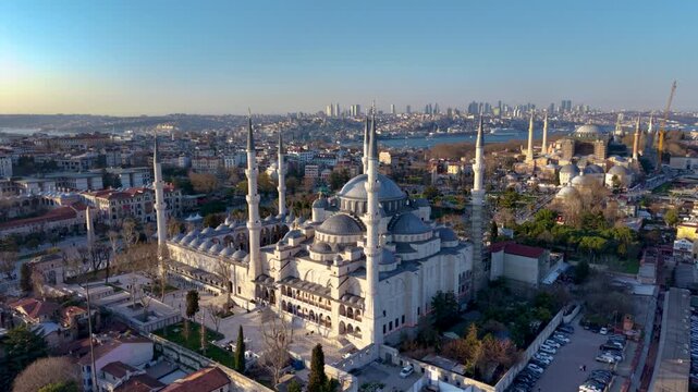 Spectacular aerial drone view of the Blue Mosque (Sultan Ahmed Mosque) in Istanbul, Turkey, with Hagia Sophia, the Bosphorus, and the modern city skyline in the background. Golden hour lighting highli