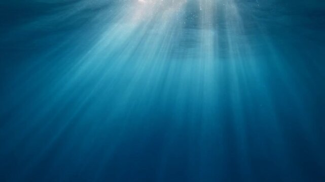 Soft underwater light rays filter through clear blue water as tiny bubbles and particles drift upward, creating calming caustic patterns with serene aquatic atmosphere.