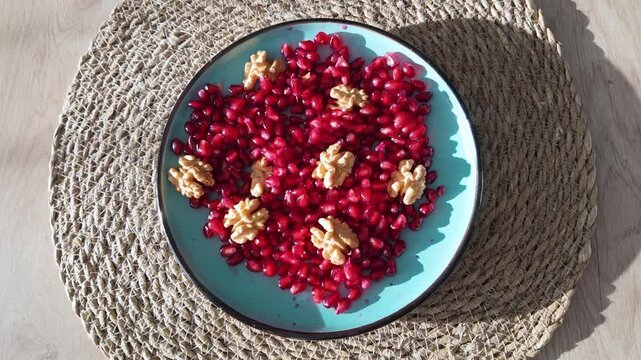 Fresh pomegranate seeds topped with walnut halves served on teal plate in bright natural light.