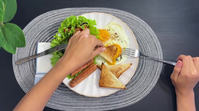 High angle footage of hand holding a fork and taking food from a breakfast plate. Concept of morning routine, eating process, tasty breakfast, food blog, morning meal, and lifestyle video. Real-time m